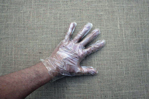 A clear plastic disposable glove displayed on a human hand, against a textured background.