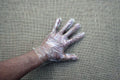 A clear plastic disposable glove displayed on a human hand, against a textured background.