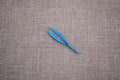 A pair of blue plastic forceps laid on a brown textured surface.