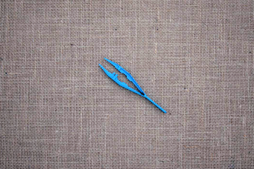 A pair of blue plastic forceps laid on a brown textured surface.