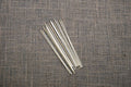 A bundle of fine wooden dissecting probes laid out on a textured grey surface.