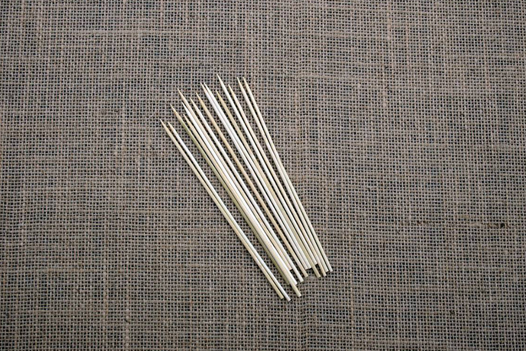 A bundle of fine wooden dissecting probes laid out on a textured grey surface.